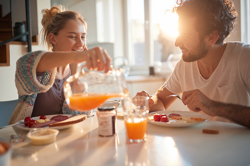 A couple eating breakfast, with sun coming through the window behind them.