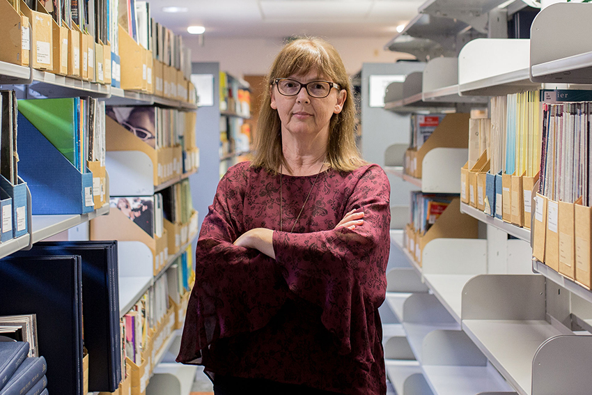 Julienne Molineaux standing arms crossed amongst library shelves.
