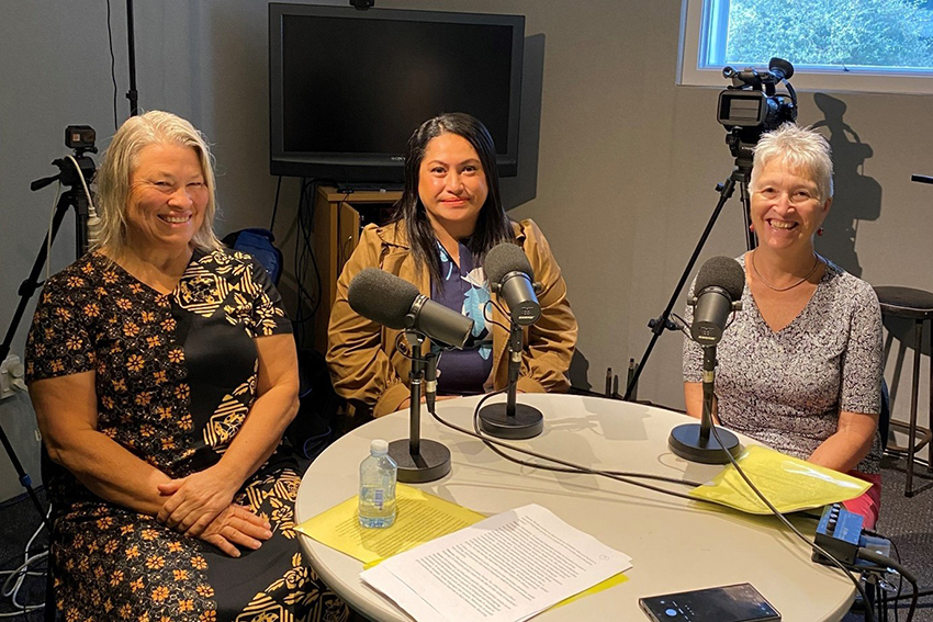 Sharon, Lanuola and Susan siting around a table with microphones, smiling.
