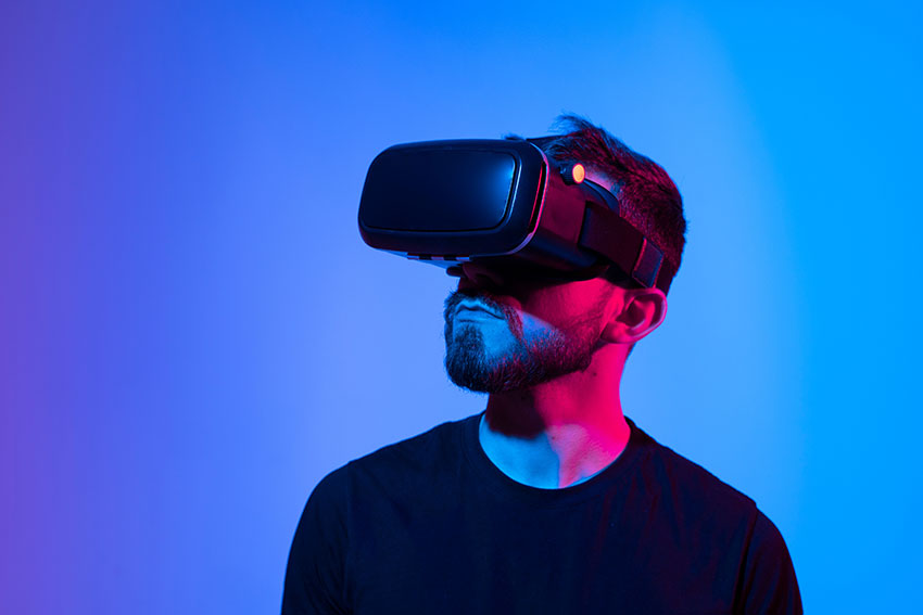 Amazed young bearded man, wearing high tech smart vr goggles, watching 360 degree video or playing a video game in metaverse.