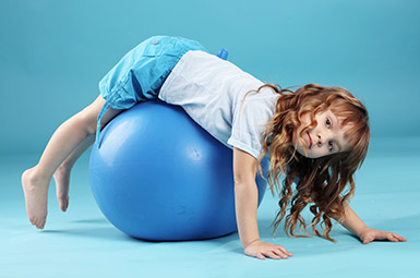 young child stretching over yoga ball